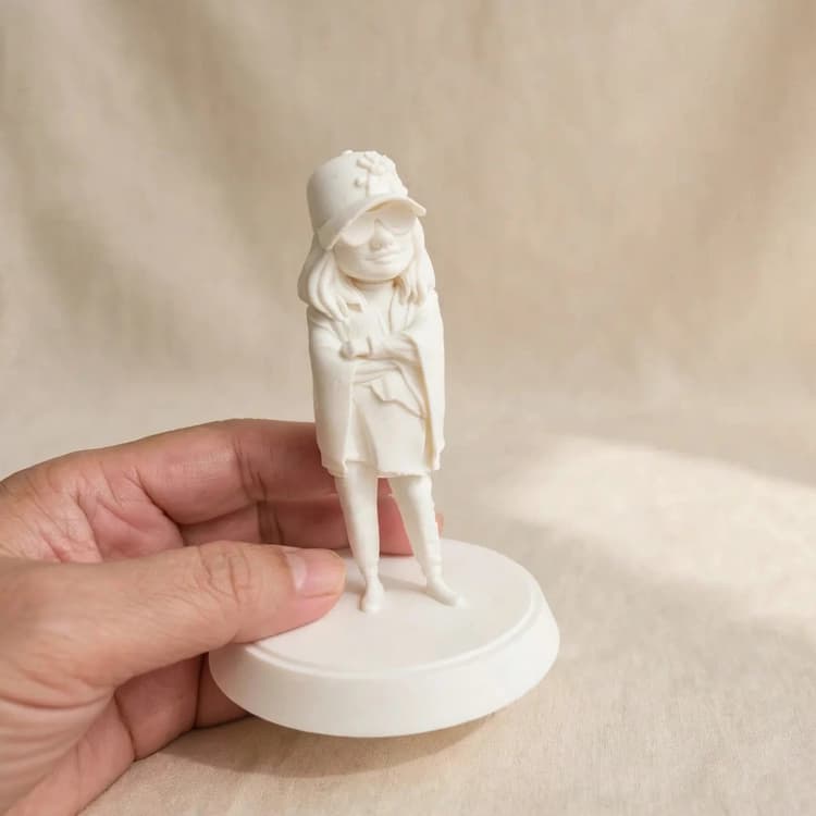 A raw white Mini Me figurine held in hand, ready to paint at home